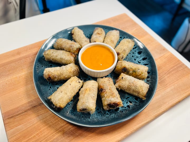 A blue plate of crispy lumpia arranged around a small bowl of peach mango ketchup.