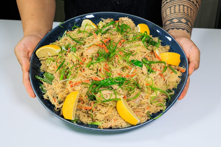 Pancit bihon on a large plate, garnished with green onions and lemon wedges.